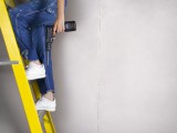Person in overalls on ladder with drill